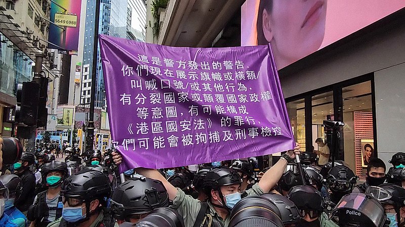 Police officer holds up a purple flag warning protestors against violations of the National Security Law